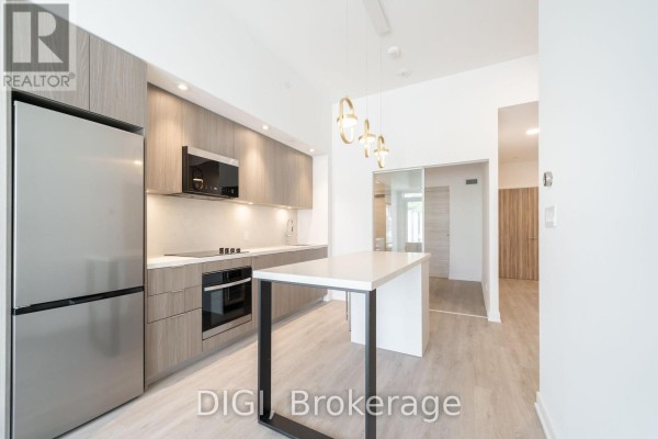 Kitchen with stainless steel refrigerator, island, wood cabinets, and doorway to hallway. - W426 - 485 Perth Avenue, Toronto