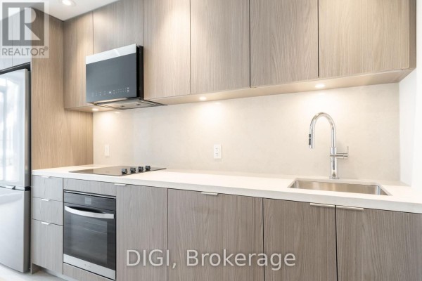Close-up of kitchen counter with stainless steel sink, faucet, stovetop, and wood cabinetry. - W426 - 485 Perth Avenue, Toronto