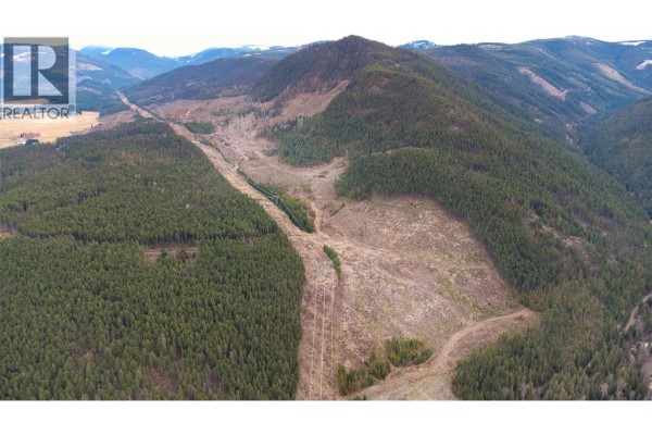 Expansive aerial view showing a cleared hillside next to a dense evergreen forest and power lines. - Walkem Road, Cherryville