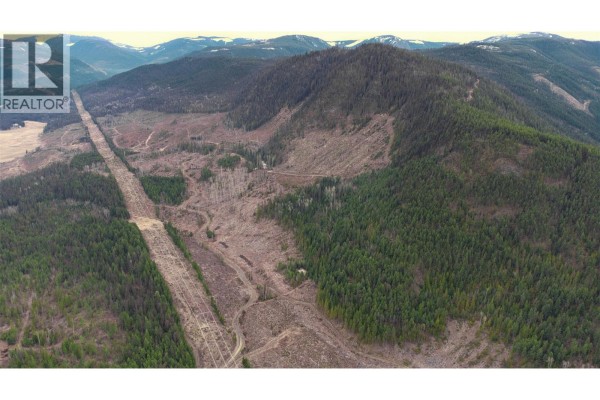Wide aerial shot of a mountainous region with partial deforestation, evergreen forest, and utility lines. - Walkem Road, Cherryville