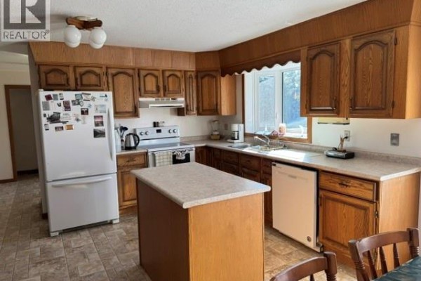 Kitchen with light oak cabinets, a breakfast island, white appliances, a window above the sink, and tiled flooring. - Wallace Acreage, Buffalo Rm No  409