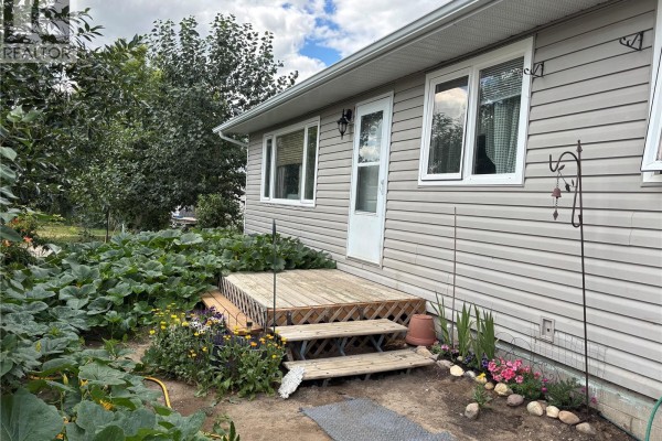 Side exterior of a house with a wooden deck and stairs surrounded by lush green plants. - Welsh Acreage, Excelsior Rm No  166
