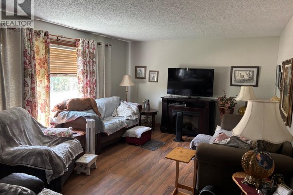 A living room with wood laminate flooring, floral curtains, a television, and a fireplace. - Welsh Acreage, Excelsior Rm No  166