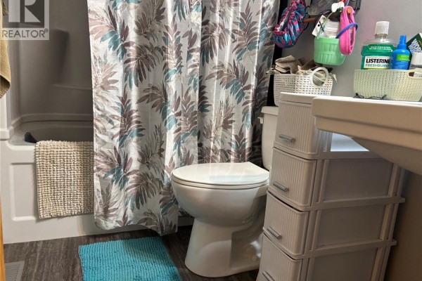 A bathroom with a white toilet, bathtub, patterned shower curtain, and white storage drawers. - Welsh Acreage, Excelsior Rm No  166
